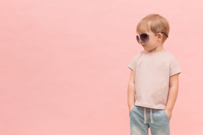 Boy wearing sunglasses standing against pink wall