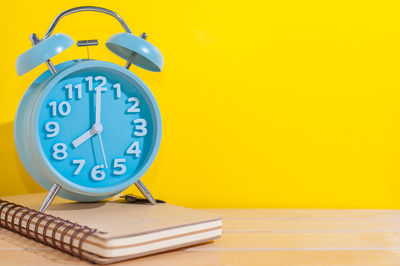 Close-up of clock on table against yellow background