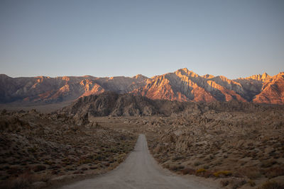 Road leading towards mountains against clear sky