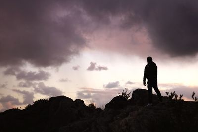 Silhouette man standing on rock against sky during sunset