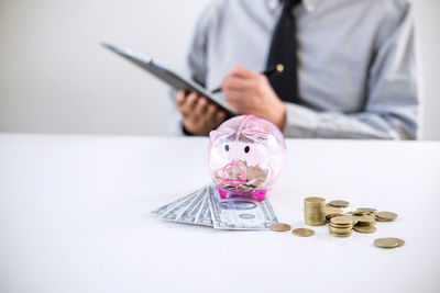 Midsection of businessman with piggy bank on table in office