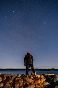 Rear view of man standing on rock at night