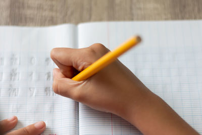 Cropped hand of child writing on book with pencil