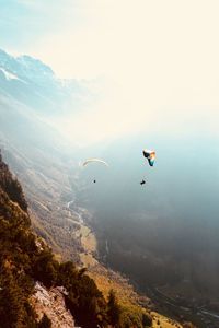 Person paragliding over mountain against sky