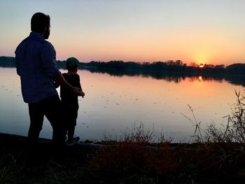 Man standing by lake against sky during sunset