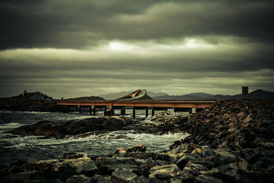 Bridge over calm sea against cloudy sky