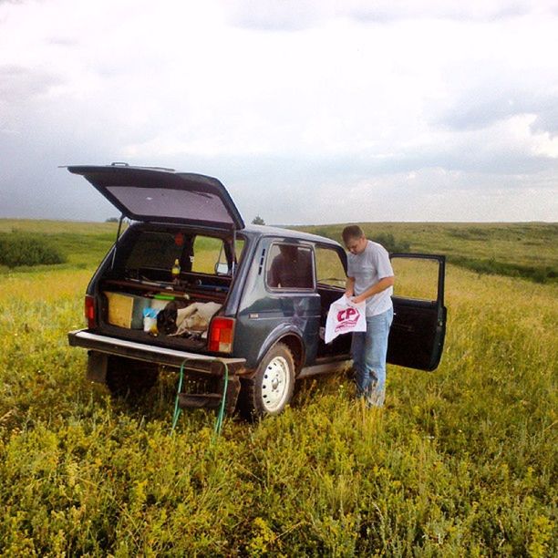 grass, lifestyles, transportation, field, sky, mode of transport, land vehicle, leisure activity, sitting, men, landscape, tractor, cloud - sky, agriculture, rear view, grassy, travel, casual clothing