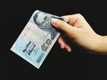 Close-up of hand holding paper over black background