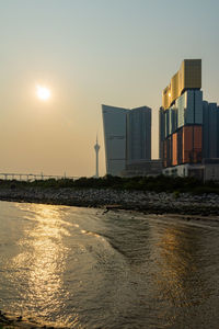 Sea by buildings against sky during sunset in city