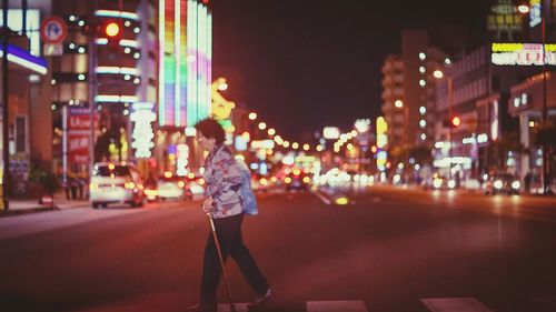 Woman standing on illuminated city street at night