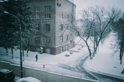 Snow covered road by buildings in city