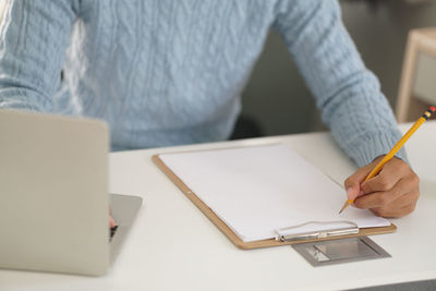 Midsection of man holding paper with text on table