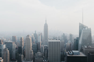 Empire state building amidst modern towers in city against sky