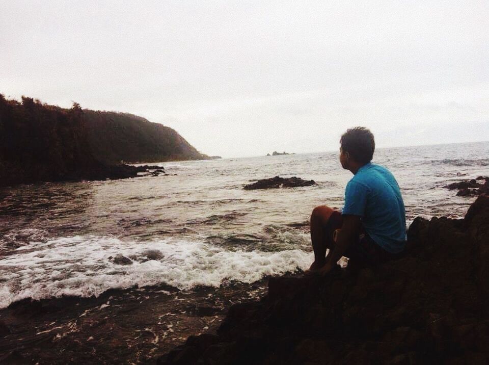 FULL LENGTH REAR VIEW OF MAN SITTING ON BEACH