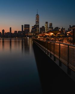 Illuminated bridge over river by buildings against sky at night