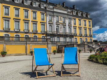 Chairs on street by building against sky