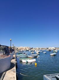 Boats moored at harbor against clear blue sky