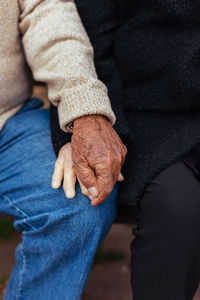 Crop of anonymous elderly couple holding hands while sitting on a park bench