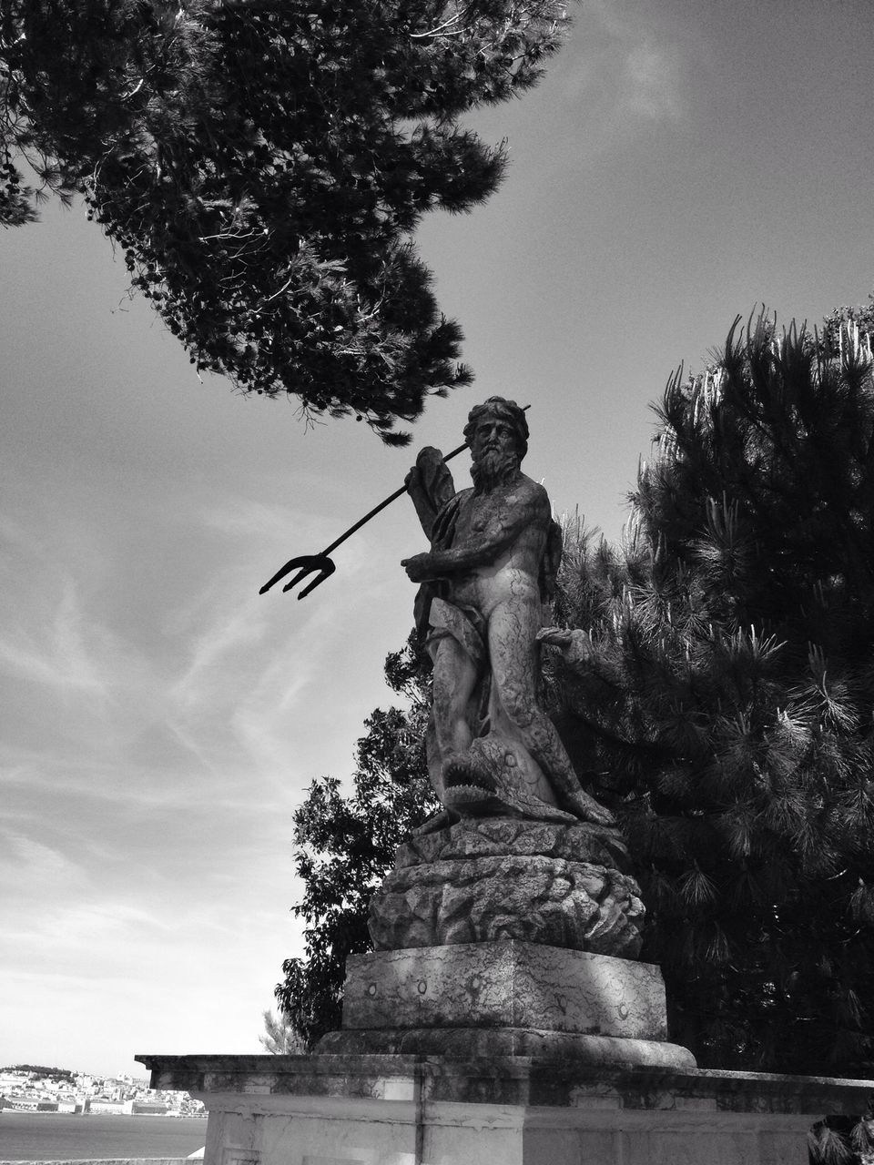 low angle view, tree, sky, growth, palm tree, sculpture, human representation, statue, nature, day, sunlight, outdoors, art and craft, one person, art, built structure, clear sky, sunbeam, cloud - sky, tranquility