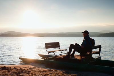 Man sitting on chair by lake against sky