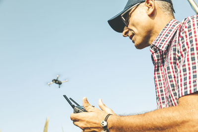 Man flying drone while standing against clear sky