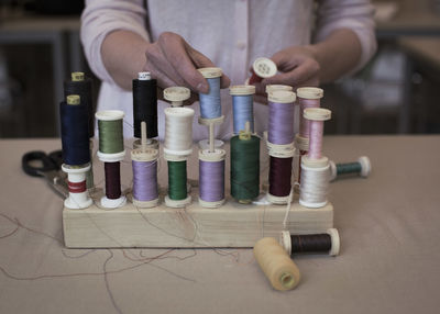 Midsection of woman putting thread spool in rack on table