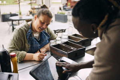 Young female owner writing down inventory while discussing with coworker at food truck