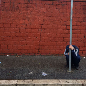 Full length of depressed man crouching against red brick wall