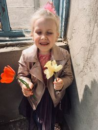 Cute girl holding flower petals standing against wall