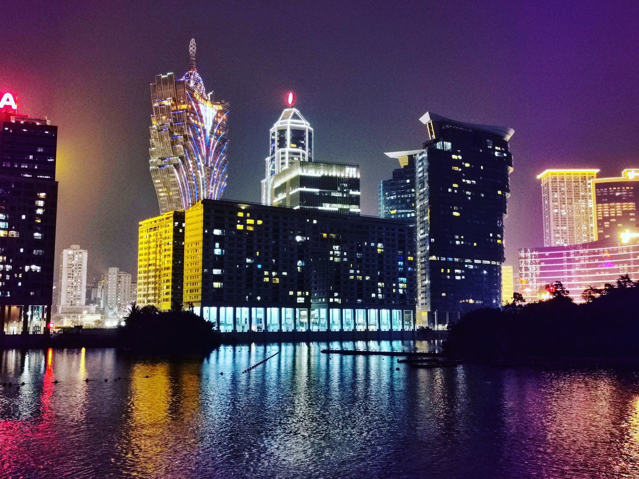 ILLUMINATED BUILDINGS BY RIVER AGAINST SKY