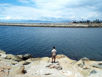 Rear view of boy standing on rock formation against sea