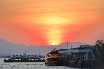 Sailboats moored at harbor against orange sky