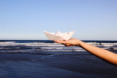 Person holding paper boat against clear sky