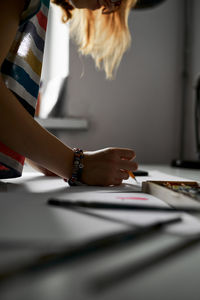 Anonymous creative woman standing at table with sketch and pencil while working on project