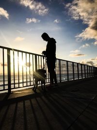 Silhouette man standing on railing against sky