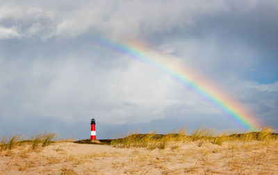 Lighthouse under rainbow at hörnum, sylt - rainy weather at dune landscape with special light