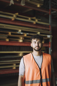 Portrait of confident young carpenter in reflective clothing at workshop