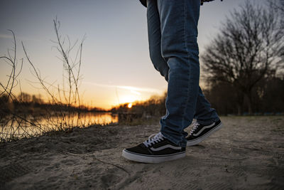 Low section of man standing on land against sky during sunset