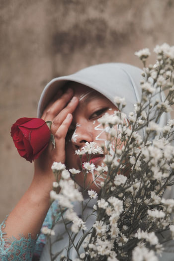 Woman wearing hijab holding flowers while standing against wall