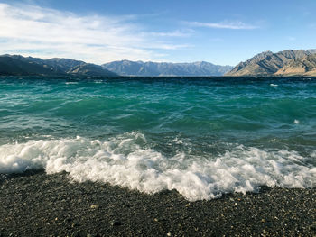 Low angle view of a green lake from its shore with a mountain range in the background.