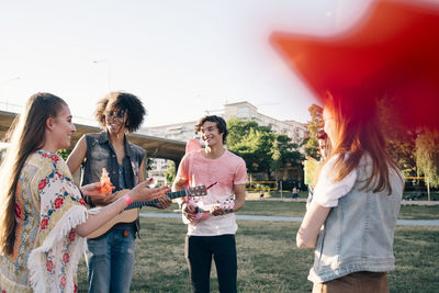 Friends talking while playing ukulele at music festival during summer