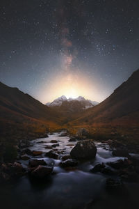 Milky way over snowy mountains and mountain river at night. landscape with high cliffs covered with