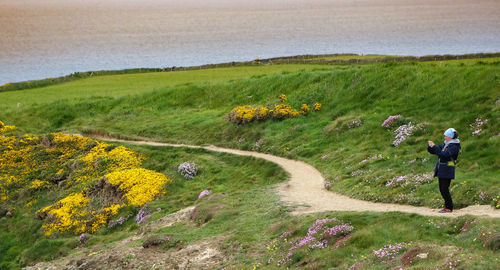 Woman photographing field while standing on footpath 