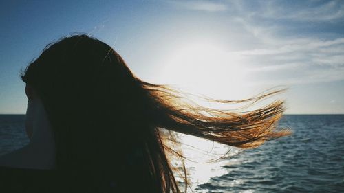 Rear view of woman with blowing hair against sunset sky