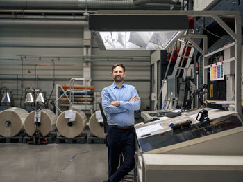 Businessman standing with arms crossed by machinery in factory