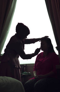 Side view of woman sitting on window