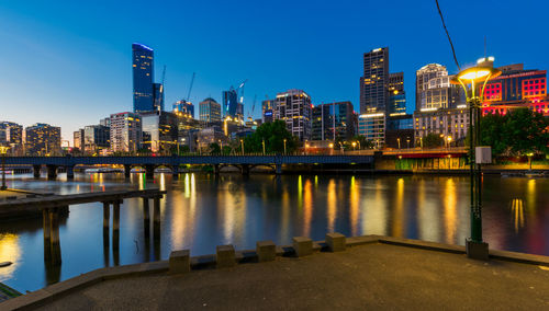 River by illuminated buildings against blue sky at dusk