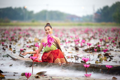 Smiling young woman holding water lilies in boat on lake