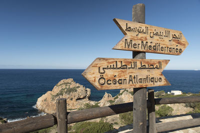 Information sign on wooden post by sea against sky