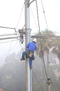 Man working on electricity pylon against sky